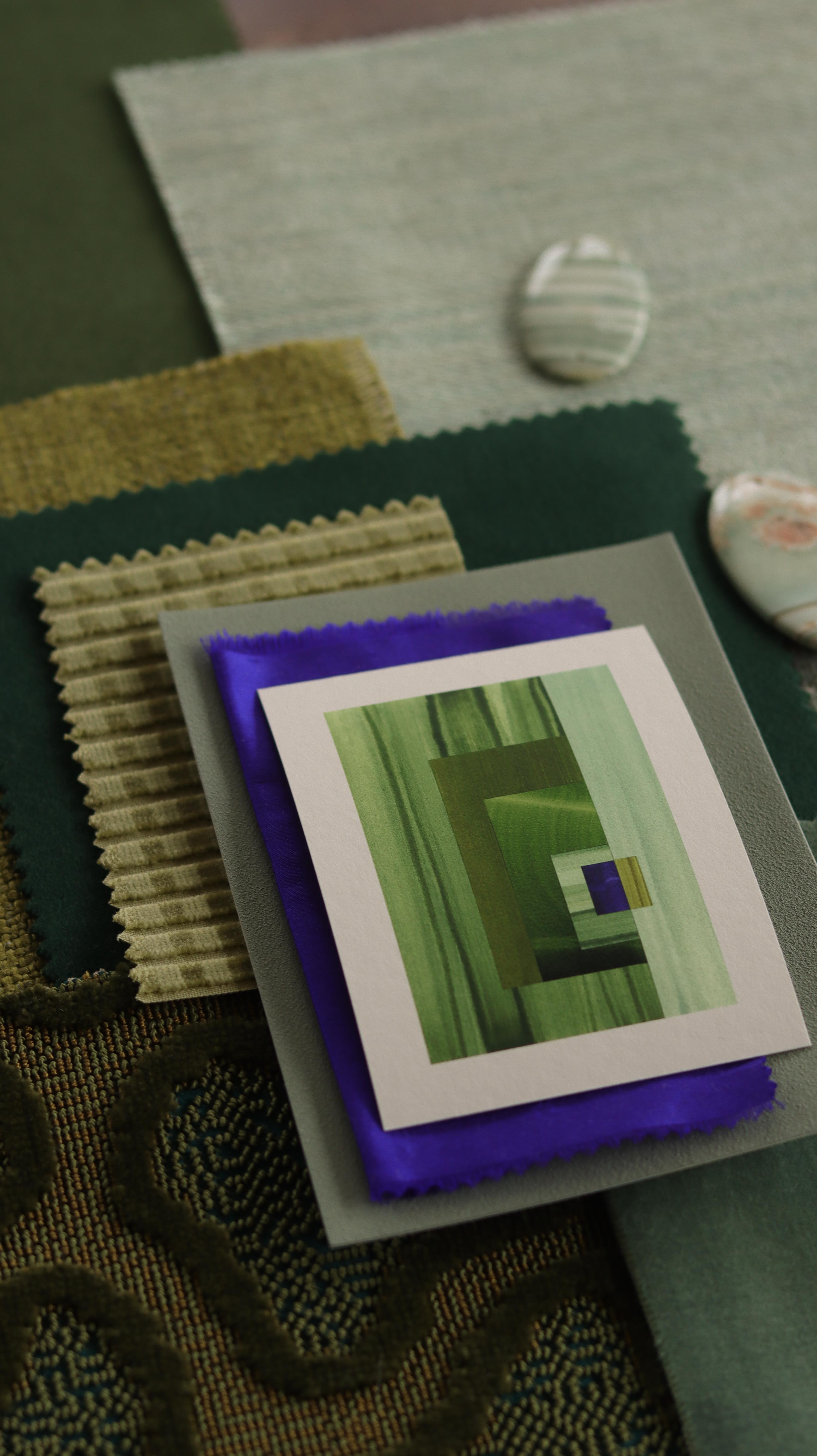 Small abstract art print sample with moss green, grass green and blue colours, laying on top of fabric swatches for green interiors colour inspiration.