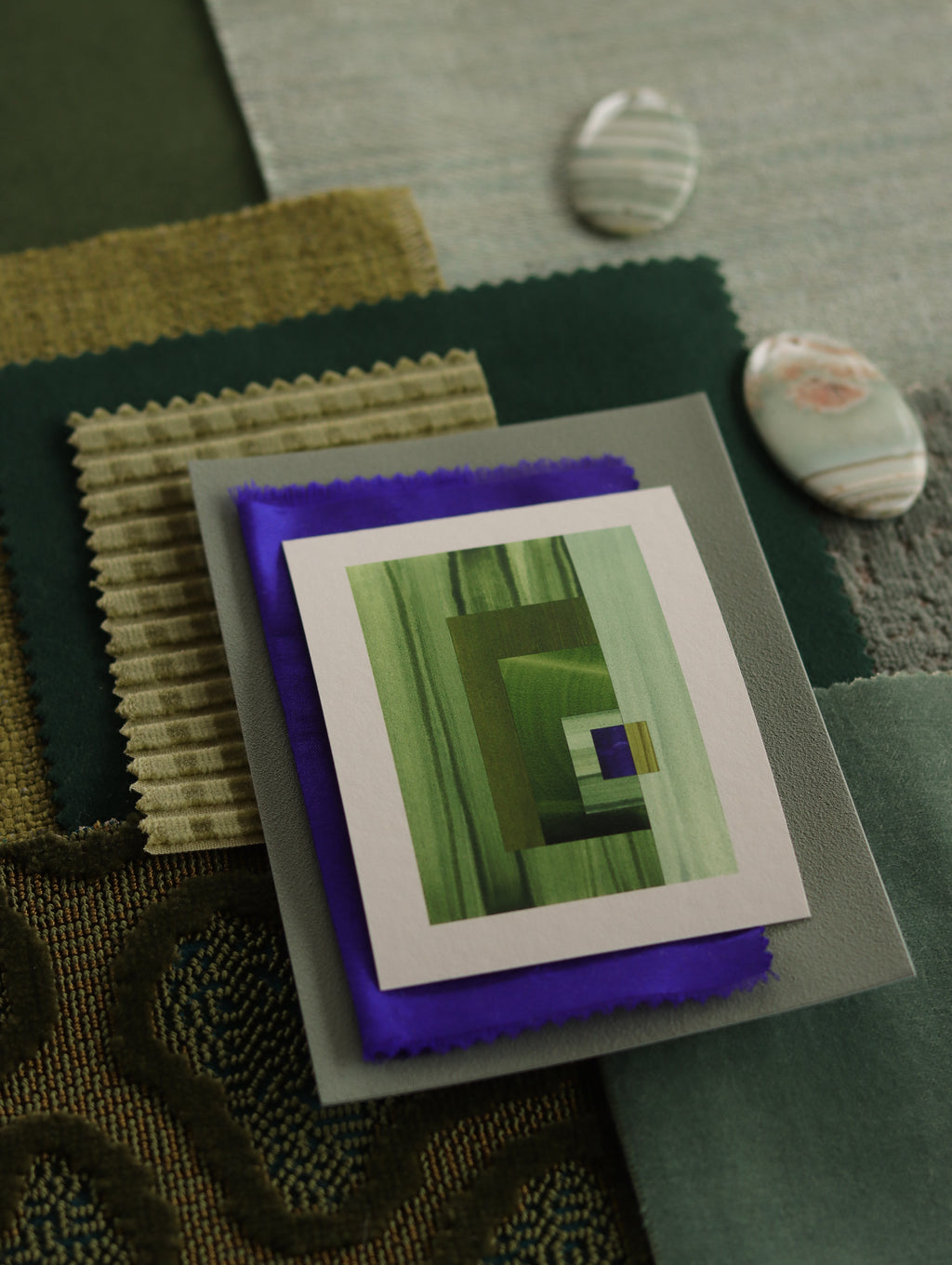 Small geometric abstract art print sample with grass green, mint green and blue colours, laying on top of fabric swatches for green interiors colour inspiration.
