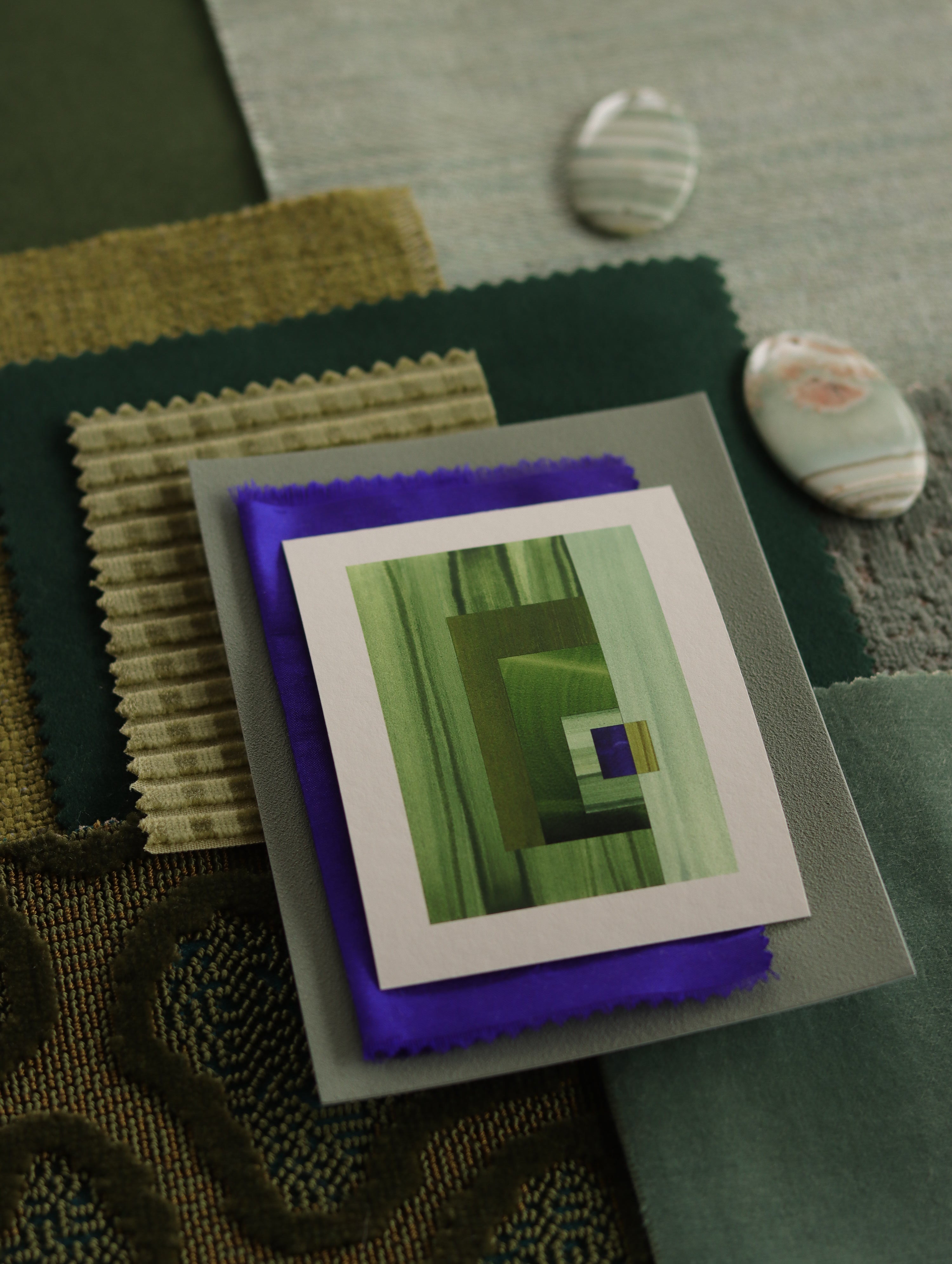 Small geometric abstract art print sample with grass green, mint green and blue colours, laying on top of fabric swatches for green interiors colour inspiration.