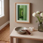 Framed green abstract artwork on a white oak console table, in a modern hallway, with a case of white flowers