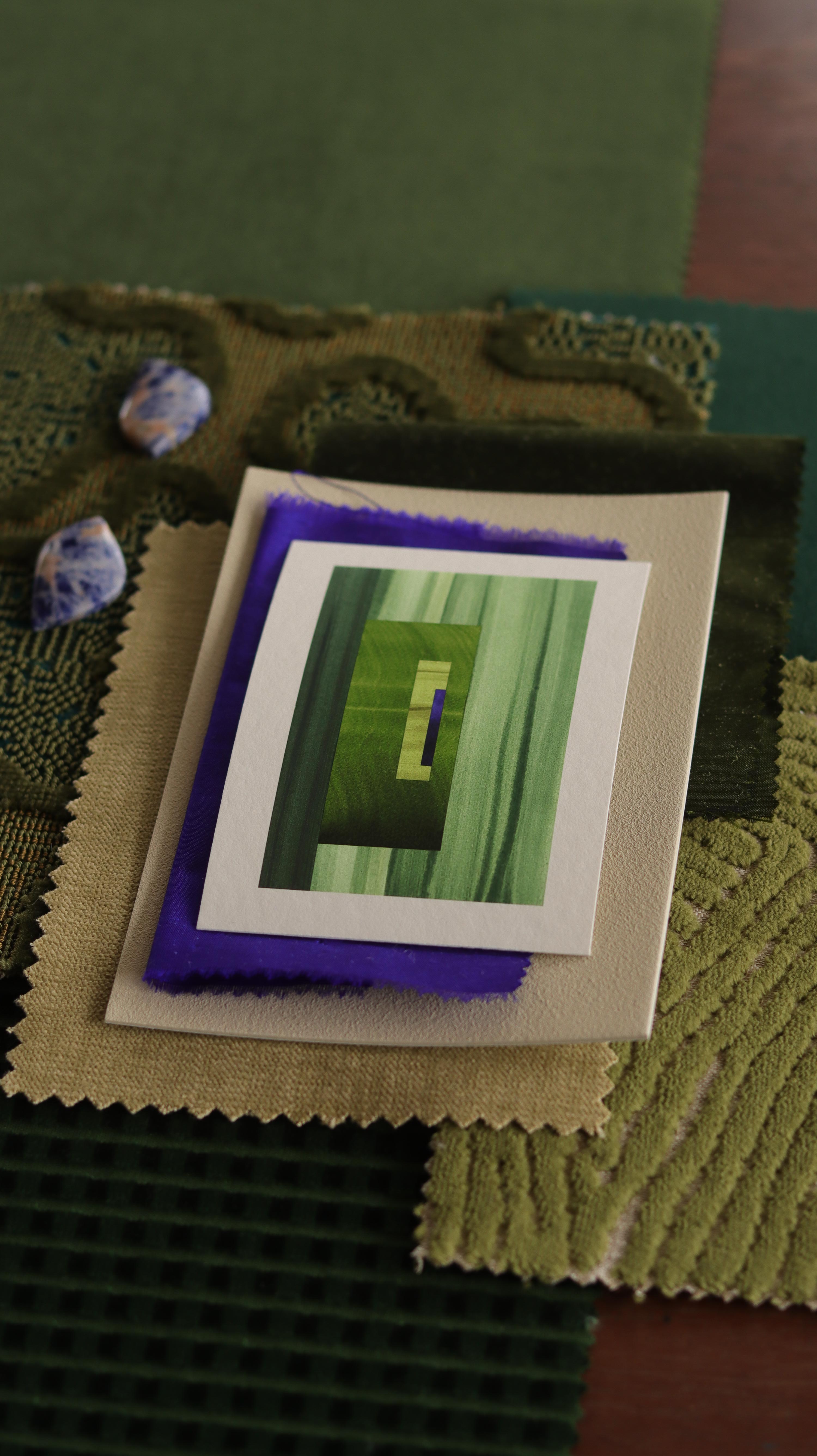 Small abstract art print sample with moss green, grass green and blue colours, laying on top of fabric swatches for green interiors colour inspiration.