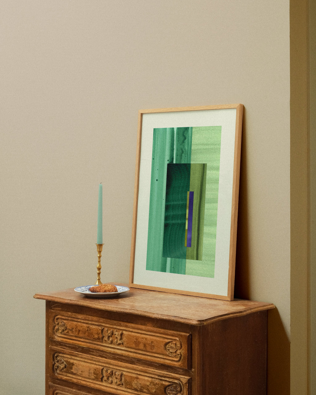Framed green abstract artwork on a wooden dresser against a beige wall