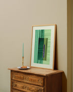 Framed green abstract artwork on a wooden dresser against a beige wall