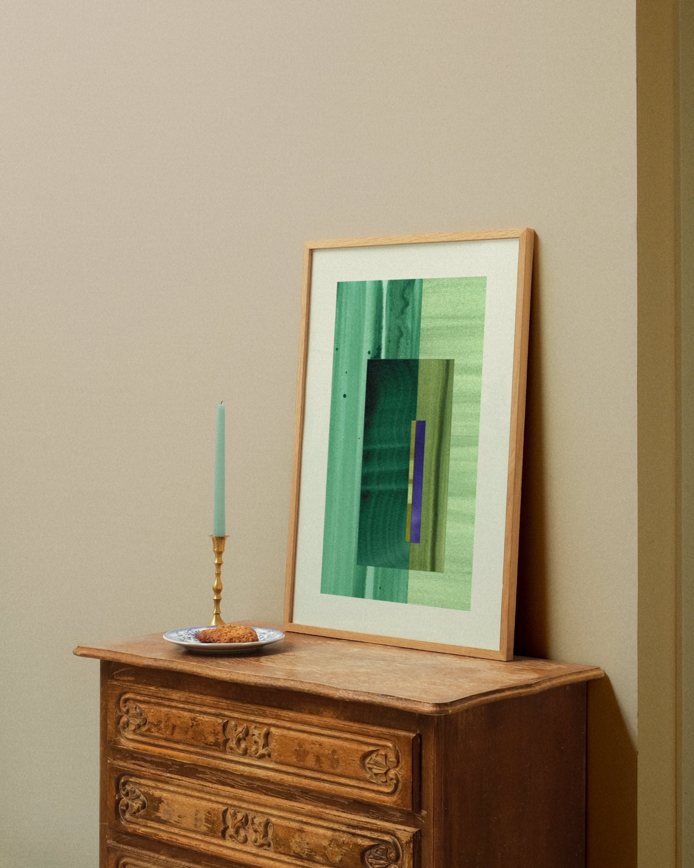 Framed green abstract artwork on a wooden dresser against a beige wall