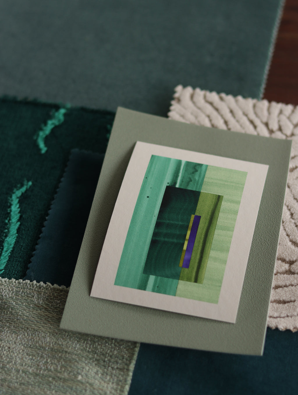 Small abstract art print sample with turquoise, forest green and blue colours, laying on top of fabric swatches for teal interiors colour inspiration.