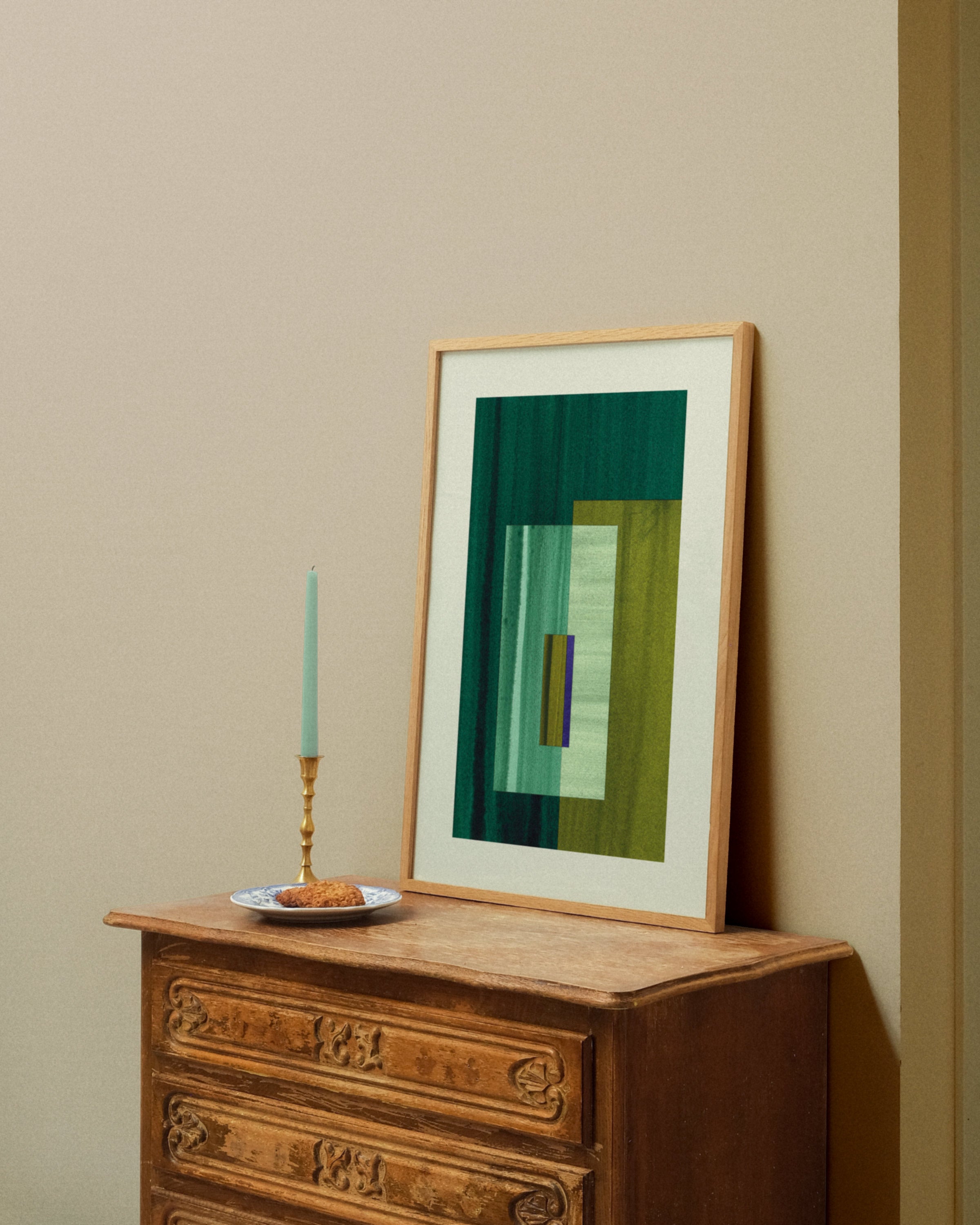 Framed green abstract artwork on a wooden dresser against a beige wall