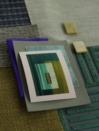 Small geometric abstract art print sample with turquoise, forest green and blue colours, laying on top of fabric swatches for green interiors colour inspiration.