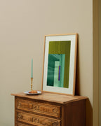 Framed moss green and turquoise abstract artwork on a wooden dresser against a beige wall