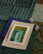Small geometric abstract art print sample with forest green, moss green  and blue colours, laying on top of fabric swatches for colourful interiors inspiration.