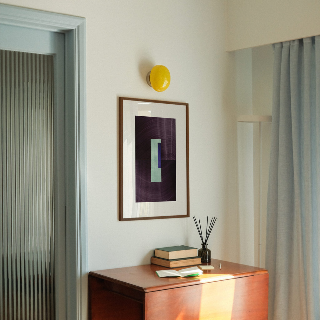 Geometric abstract art with eggplant purple, turquoise and blue colours, in a walnut frame, hung in a midcentury modern, minimal living room interior.