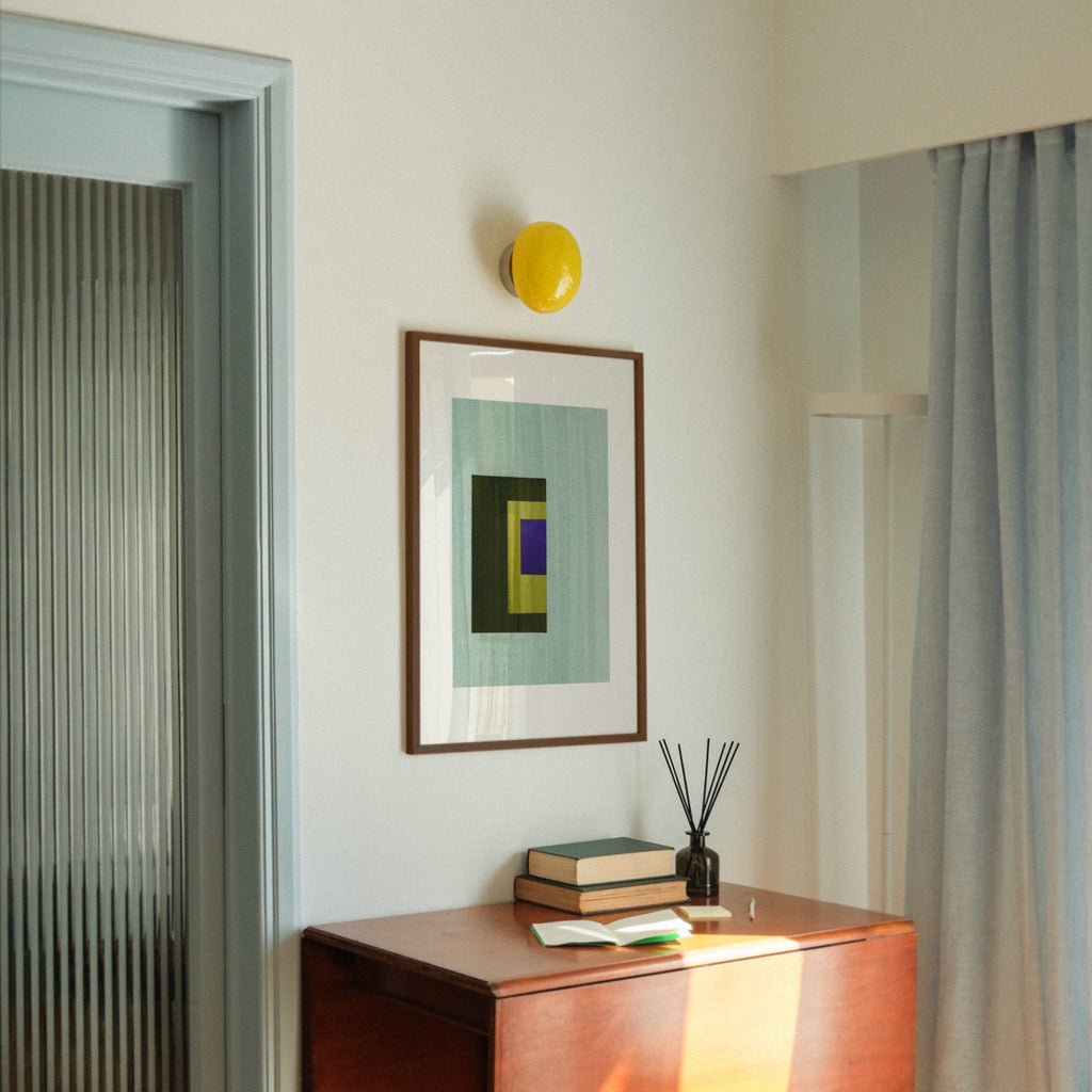 Geometric abstract art with turquoise, olive green and blue colours, in a walnut frame, hung in a midcentury modern, minimal living room interior.