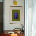 Geometric abstract art with green and blue colours, in a walnut frame, hung in a midcentury modern, minimal living room interior.