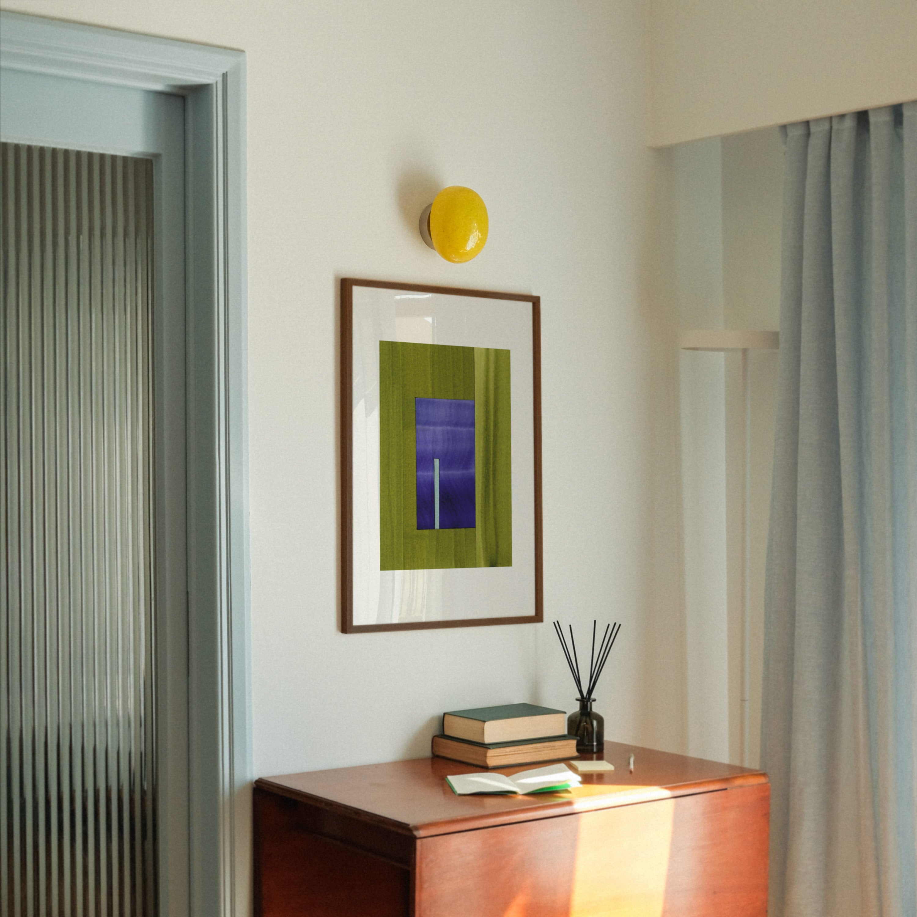 Green and blue geometric abstract art, in a walnut frame, hung in a midcentury modern, minimal living room interior.