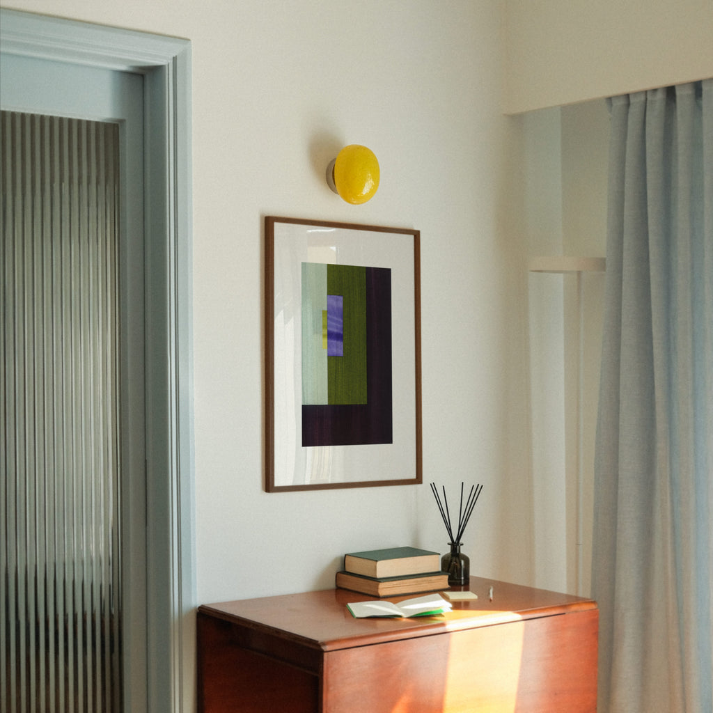 Geometric abstract art with green, dark brown, olive green and blue colours, in a walnut frame, hung in a midcentury modern, minimal living room interior.