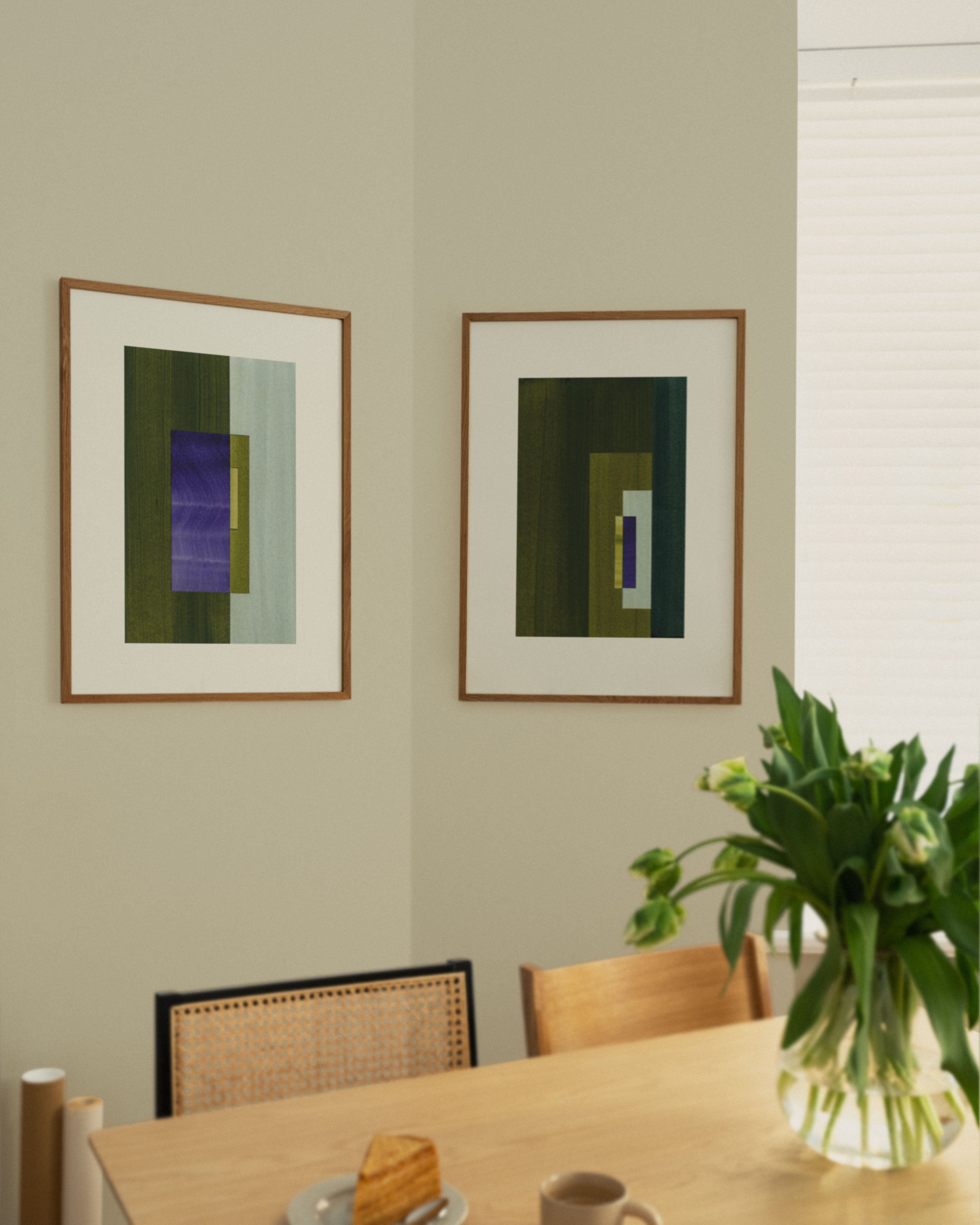 Two framed minimalist abstract artworks framed on a wall above a dining table in a modern kitchen with tulips.